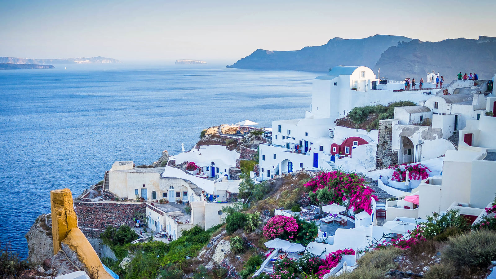 Hvide huse og blaa kupler i Oia paa Santorini med calderaen bagved